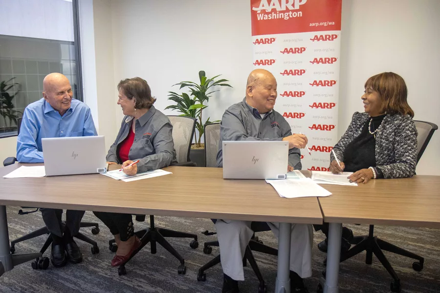 Four people sitting at a desk with an AARP sign.