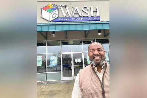 Man standing outside a laundromat called, "The Wash".