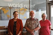 Three people standing by a window that reads, "World Relief Tri-Cities".