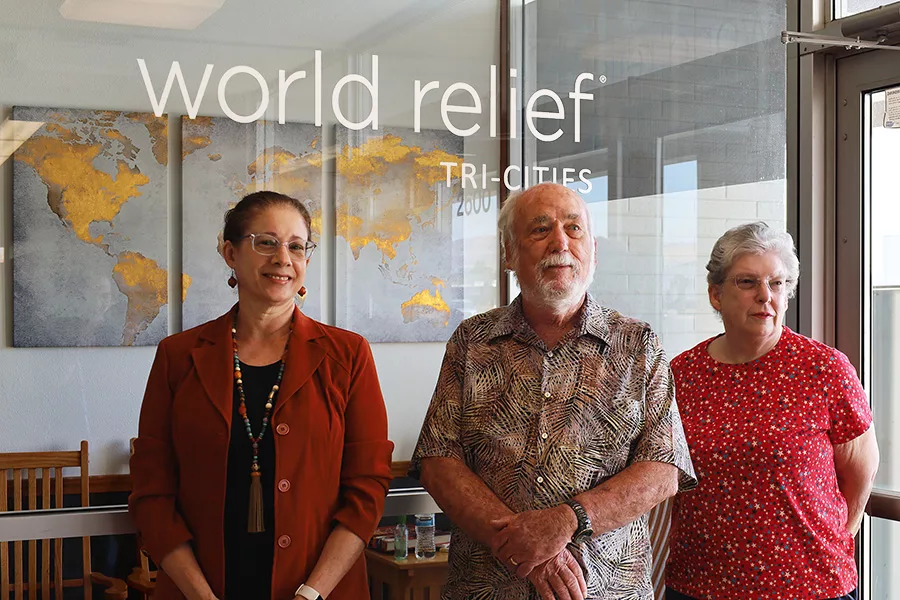 Three people standing by a window that reads, "World Relief Tri-Cities".