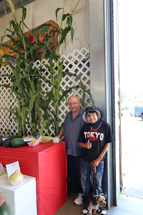 Two people and a dog near cornstalks.