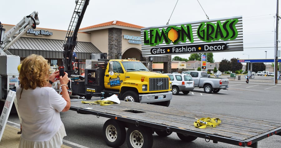 Lemon Grass Gifts owner Linda Pasco snaps a photo while a new sign for her store is installed at Marineland Plaza at 5215 W. Clearwater Ave. in Kennewick. A major remodel of the 30-year-old retail plaza has encouraged businesses to move in and longtime tenants to make improvements.