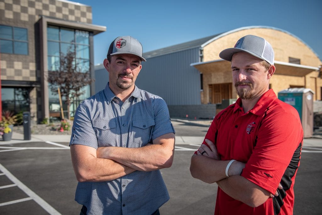 Brothers Jake and Josh Musser stand in front of the new Trucks & Auto Auctions at 3135 Rickenbacker Drive in the Port of Pasco’s Tri-Cities Airport Business Center. A new $10 million, four-story Courtyard by Marriott hotel is under construction in the center. (Photo: Scott Butner Photography)