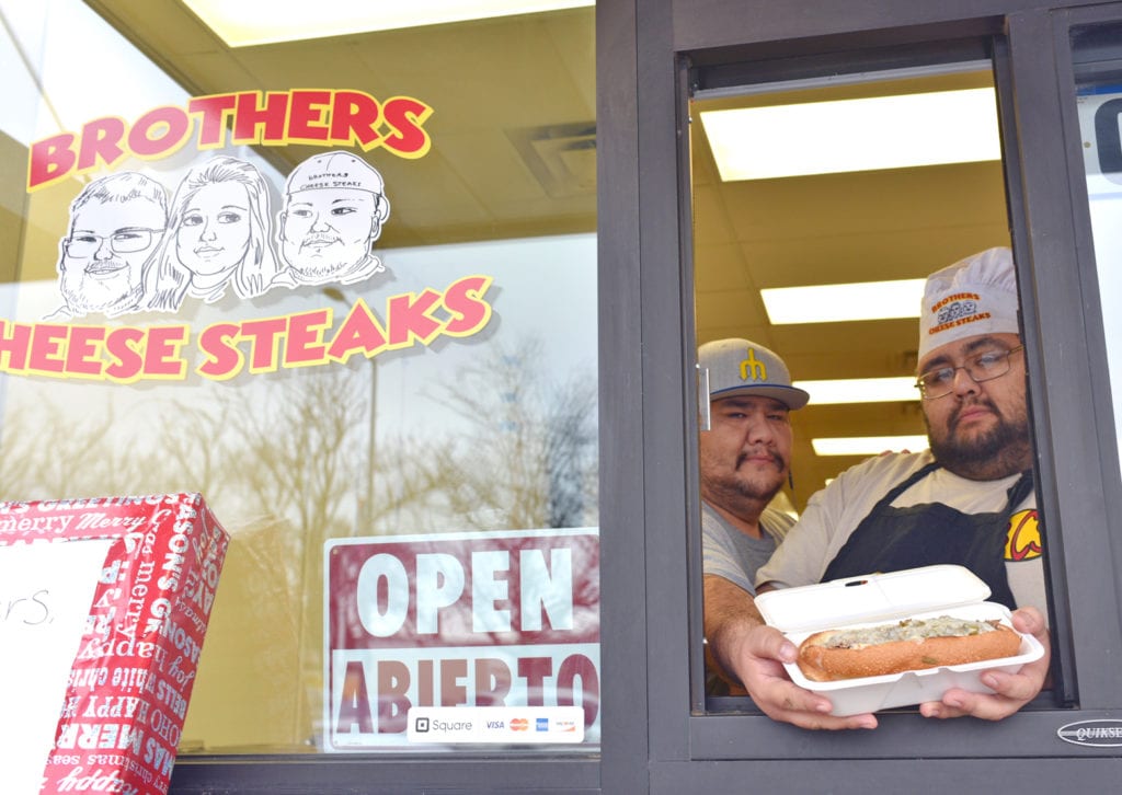 Mario and Coco Quintero pose with their popular Philly cheesesteak sandwich outside in the walk-up window at the Pasco Specialty Kitchen in downtown Pasco at 110 S. Fourth Ave.