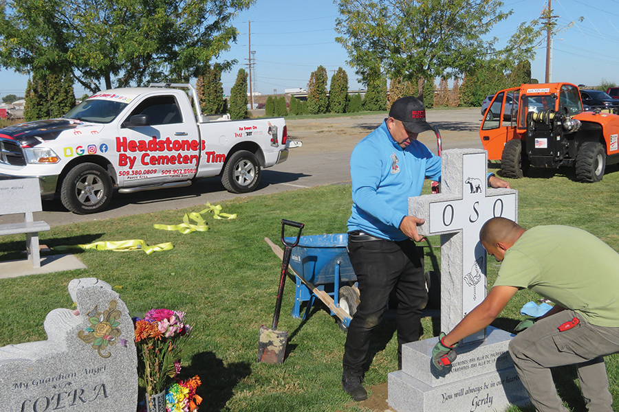 Tim Morris, owner of Headstones by Cemetery Tim, sets a headstone at Pasco’s City View Cemetery with help from Gilbert Sanchez. His eye-catching branded pickup is parked behind him. (Photo by Kristina Lord)