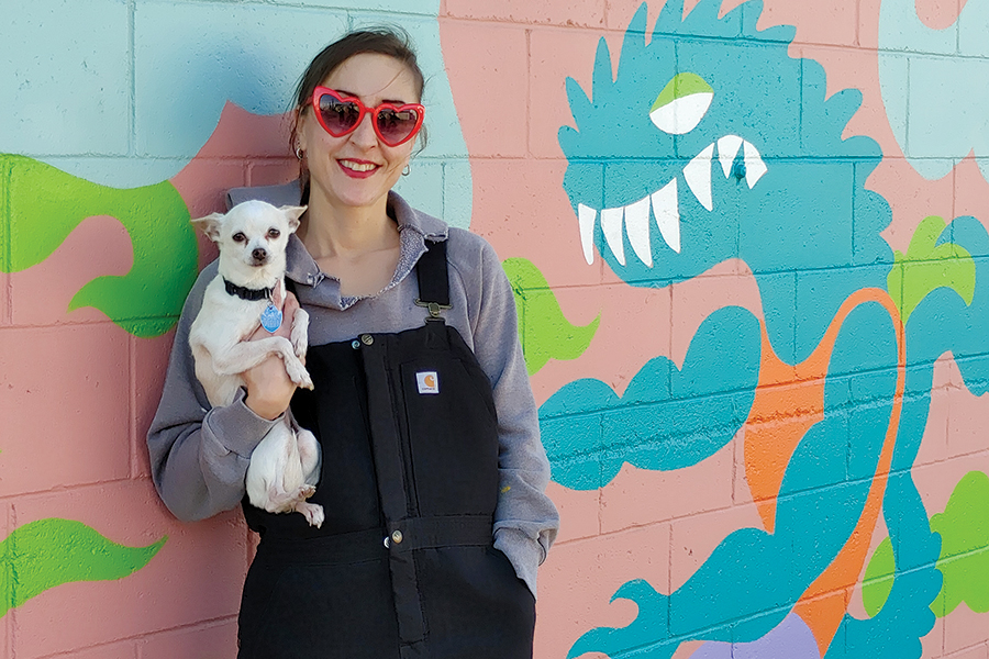 Artist Heidi Elkington and her dog, Carmen Electra, pose by her skateboard-themed mural behind Real Deals in the Uptown Shopping Center alley. Gallery in the Alley is an emerging art destination in the heart of Richland. The subject – a lizard riding a board – is a nod to Elkington’s youth, growing up in Richland and skateboarding at the shopping center. (Photo by Wendy Culverwell)