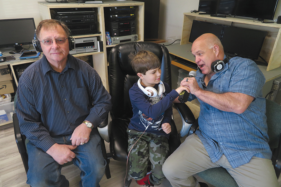 Freddy Mielke, 9, of West Richland, center, is comfortable with a microphone and on a stage. His dad, Marty Mielke, right, hopes his son will take over the family business someday. He recently bought Sight and Sound Services in Kennewick from Bob Kreider, left. (Photo by Kristina Lord)