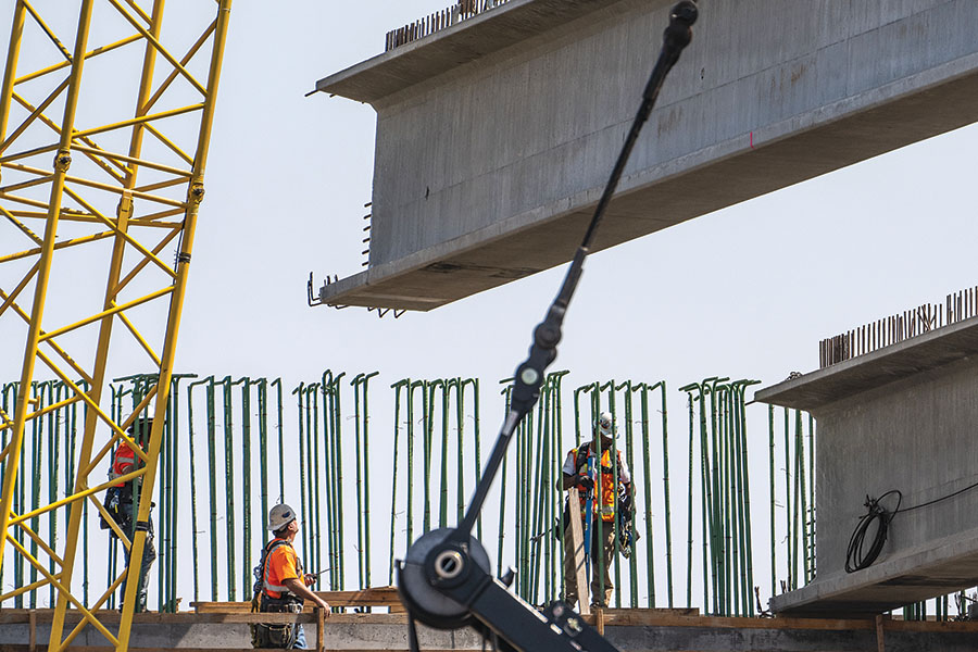 Workers guide a concrete beam into place for Pasco’s $36.2 million Lewis Street overpass project, which is expected to be completed in August or September. The overpass replaces the outdated underpass and will span the BNSF Railway yard and First Avenue. (File photo by Scott Butner Photography)